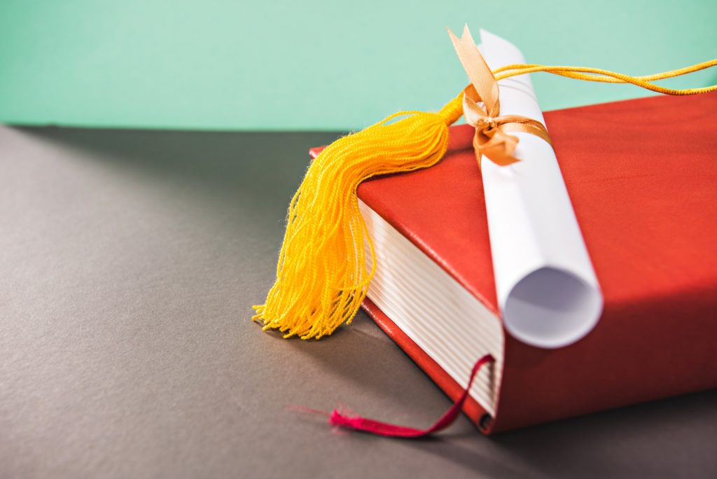 close up of books, diploma and tassel of graduation cap with copy space, education concept